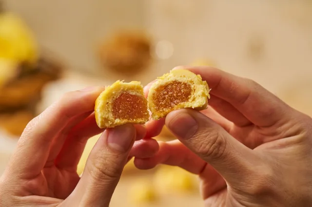 Hands holding a Pineapple Ball split open to show its pineapple filling and pastry.