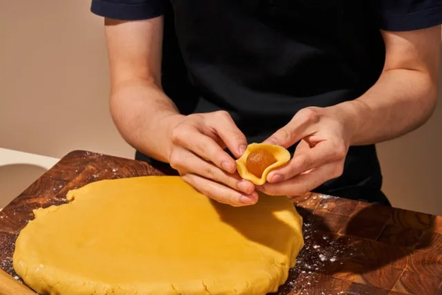 Hands shaping pastry around a pineapple filling
